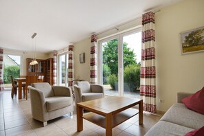 Ein Wohnzimmer mit einer Couch, Sesseln, einem Tisch und Blick durch große Fenster.