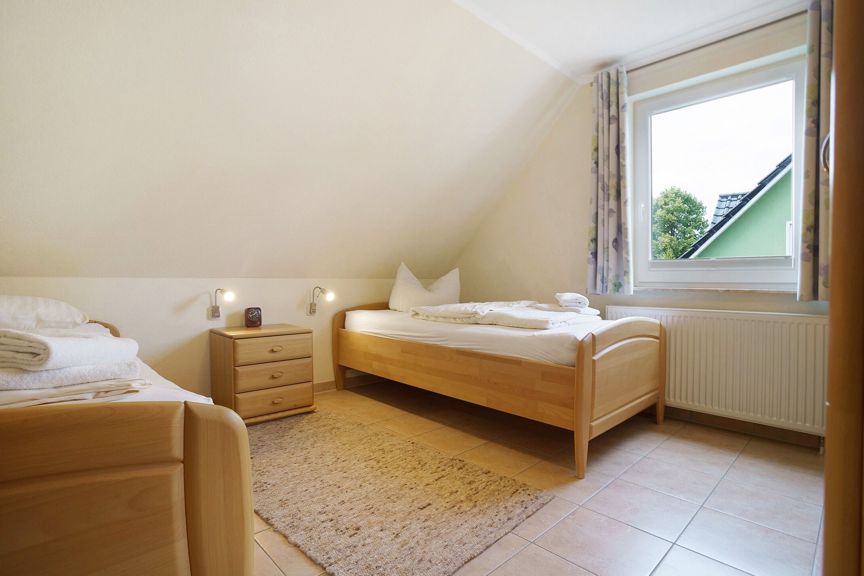 Une chambre à coucher avec un lit en bois, une table de chevet, une commode, une fenêtre avec des rideaux et un radiateur.