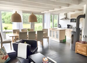 Eine moderne Küche mit Einbauherd, Essbereich mit Stühlen und Tisch, und große Fenster mit Blick auf Grünflächen.