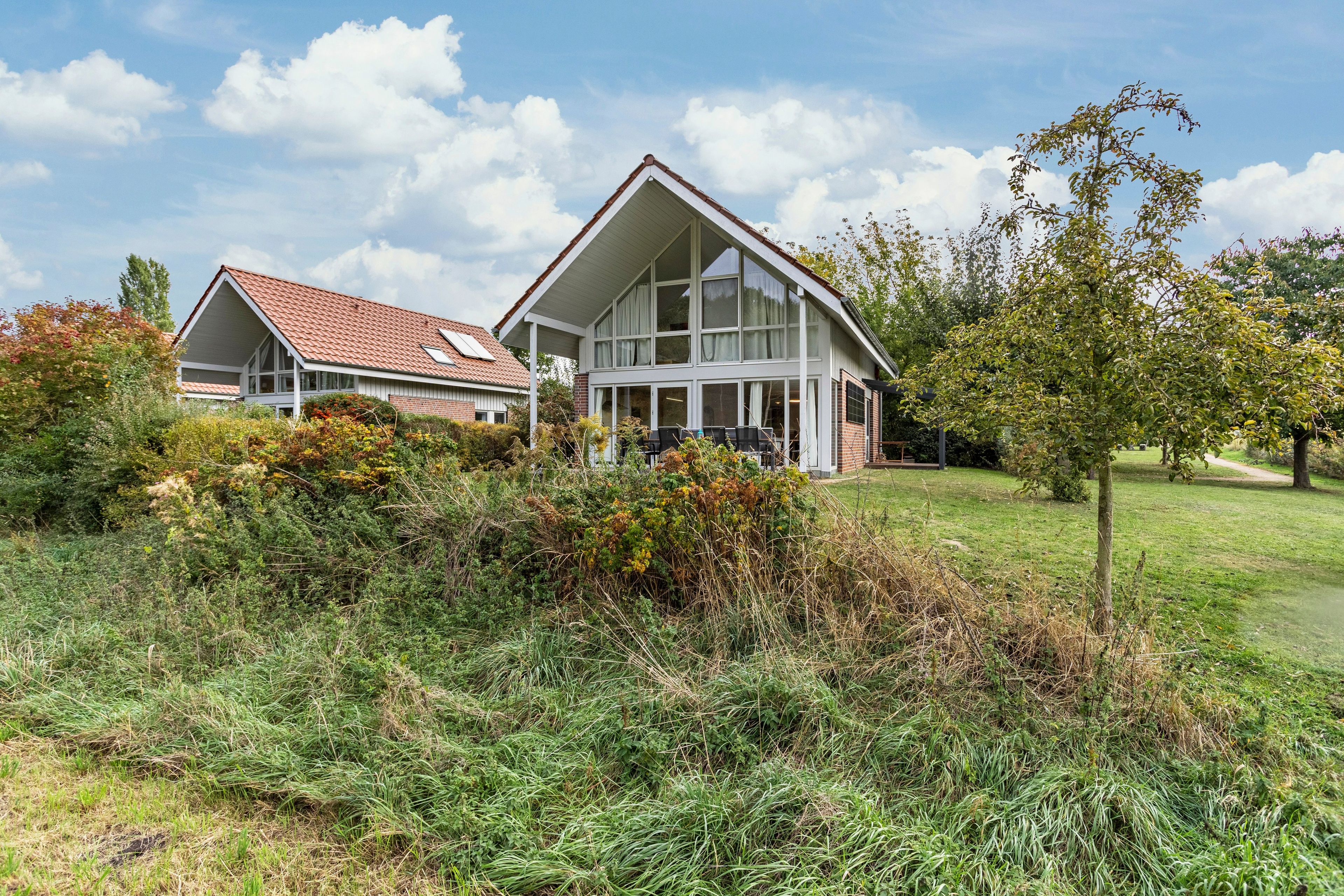 Une maison à deux étages avec un toit en pente, de grandes fenêtres et un jardin à l’avant.