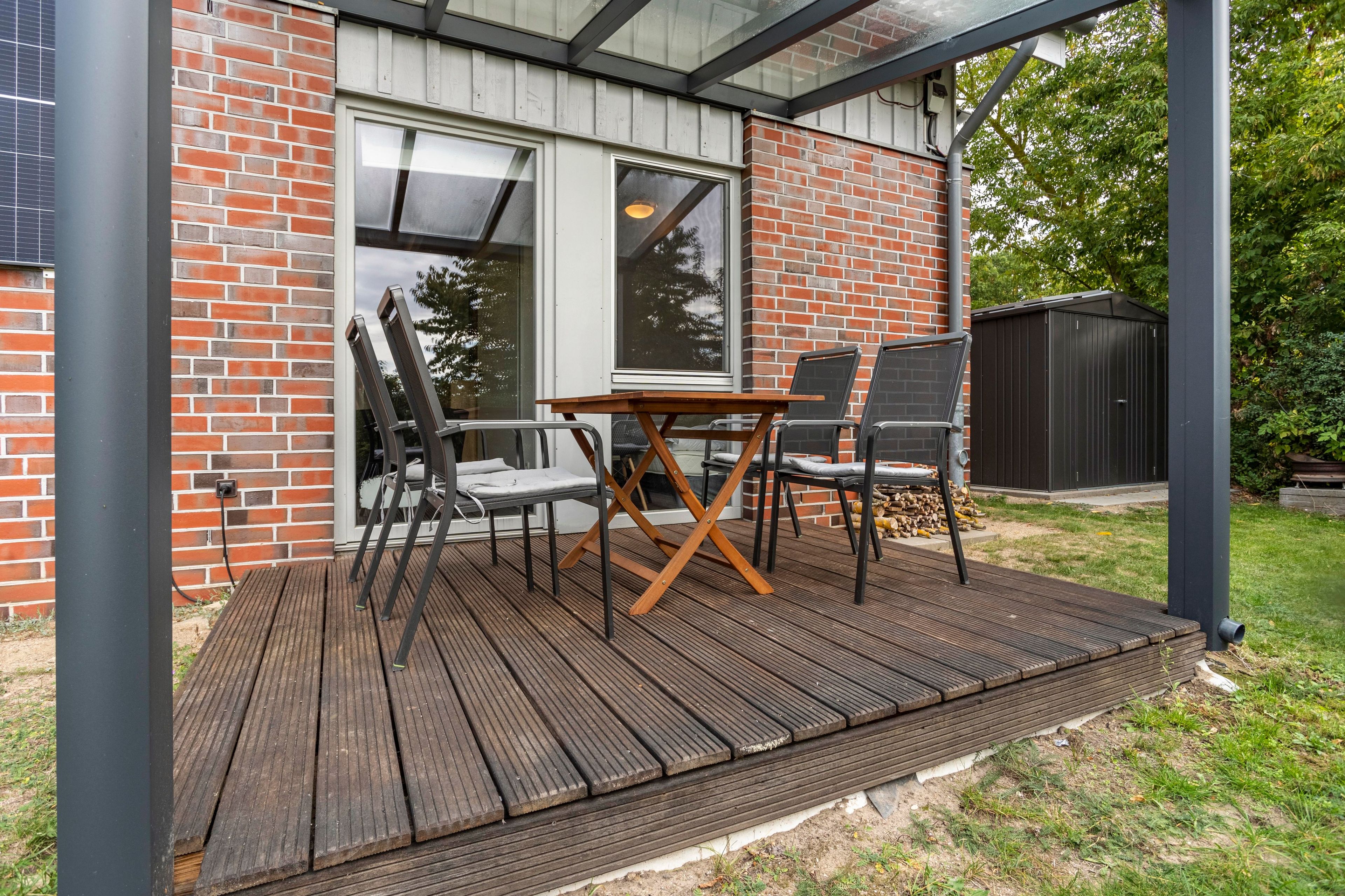 Un área de patio techada con una terraza de madera, una mesa y sillas.