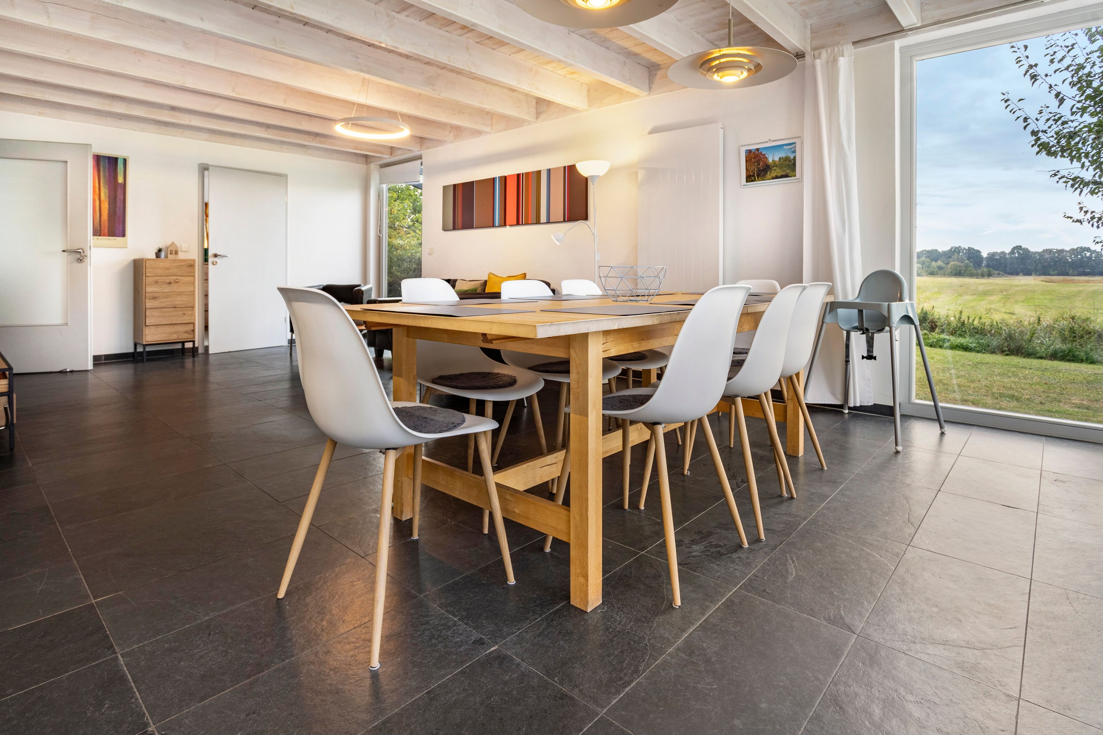 A modern dining area with a wooden table, grey chairs, and a view of the outdoors.