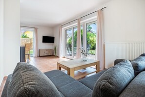 A modern living room with a sofa set, a wooden coffee table, and a TV mounted on the wall. - Holiday Home 'Haus 26' with Private Terrace, Private Garden and Wi-Fi (Röbel)