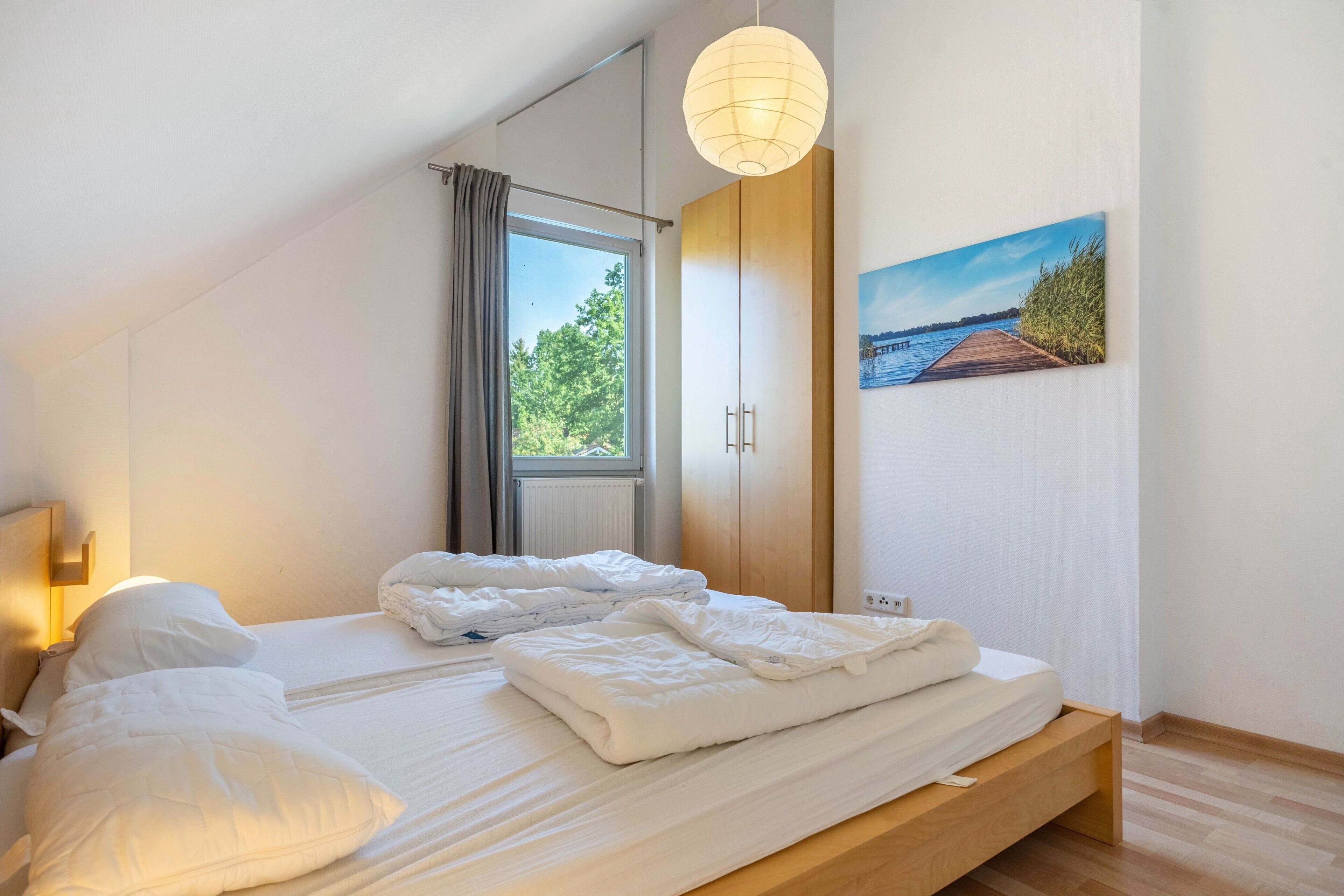 A bedroom with a bed, a window, a painting, and a wooden wardrobe.