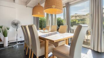 A dining area with a wooden table and chairs, large windows, and a fan.