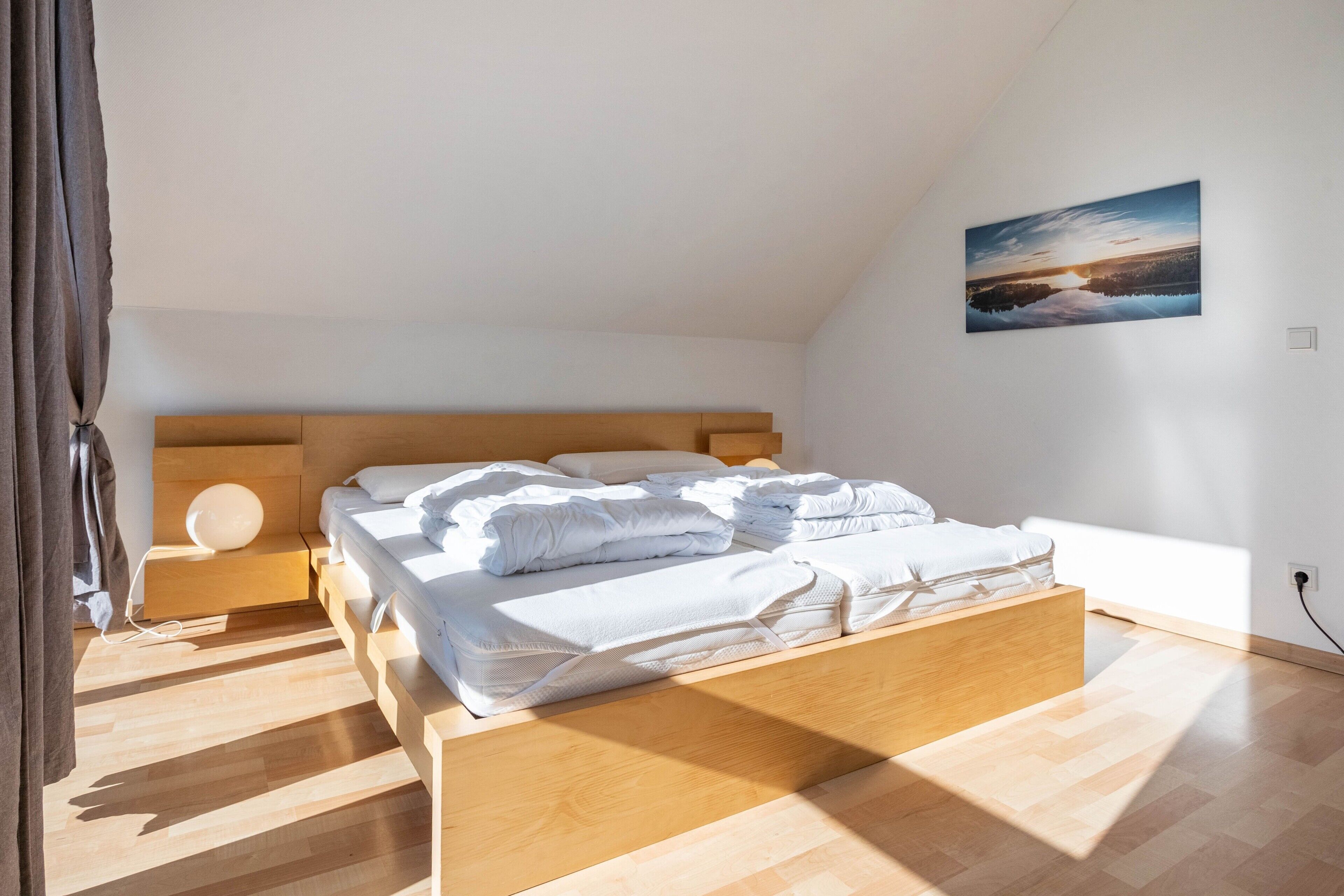 Ein Schlafzimmer mit einem hölzernen Bett, einem Nachttisch, einer Wandlampe und einem Gemälde vom Sonnenuntergang.