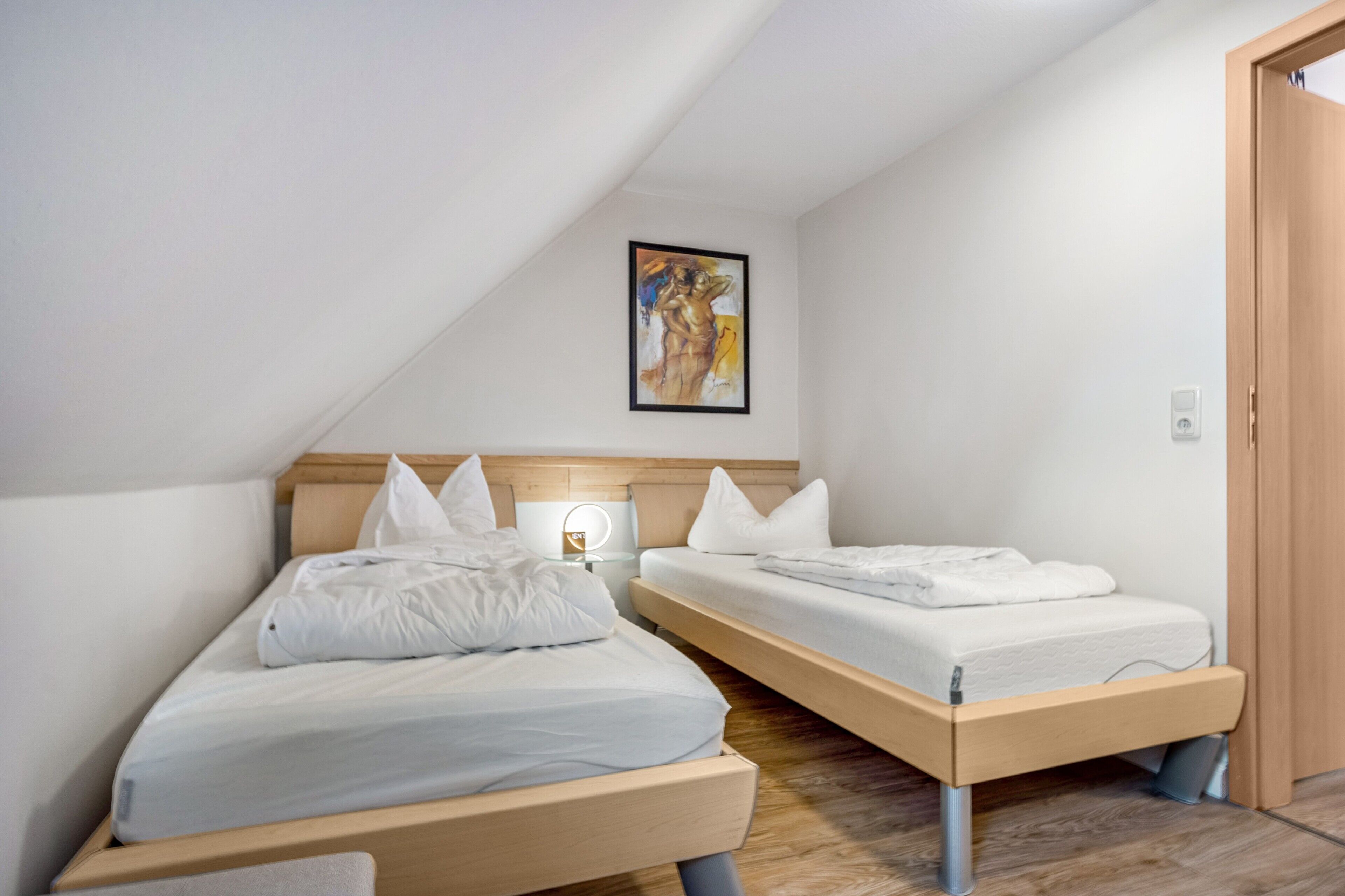 A bedroom with two single beds, a bedside table with a lamp, and a framed artwork on the wall.