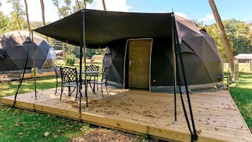 A camping site with a large tent, a dining table, and chairs.