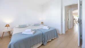 Ett hotellrum med två sängar, ett litet bord med en lampa och en dörr som leder till ett annat rum.
