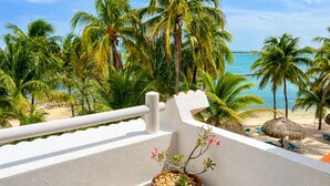 Un balcon avec vue sur une plage, des palmiers et un parasol en chaume.