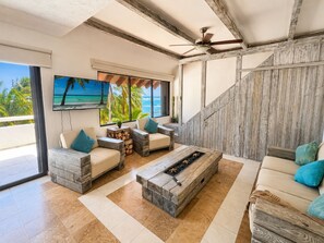A modern living room with a fireplace, comfortable seating, a television, and a view of the ocean. - Beachfront condo with loft and sea views (Puerto Aventuras)