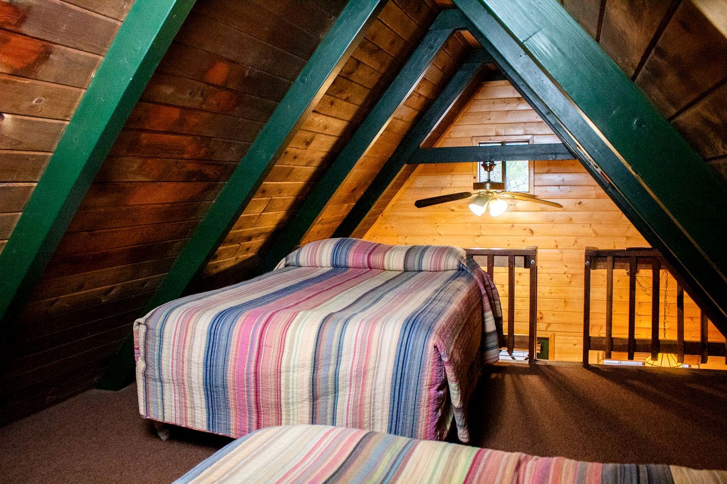 Un dormitorio acogedor en el ático, con techo inclinado, cama con ropa de cama a rayas, una mesita pequeña y un ventilador de techo.