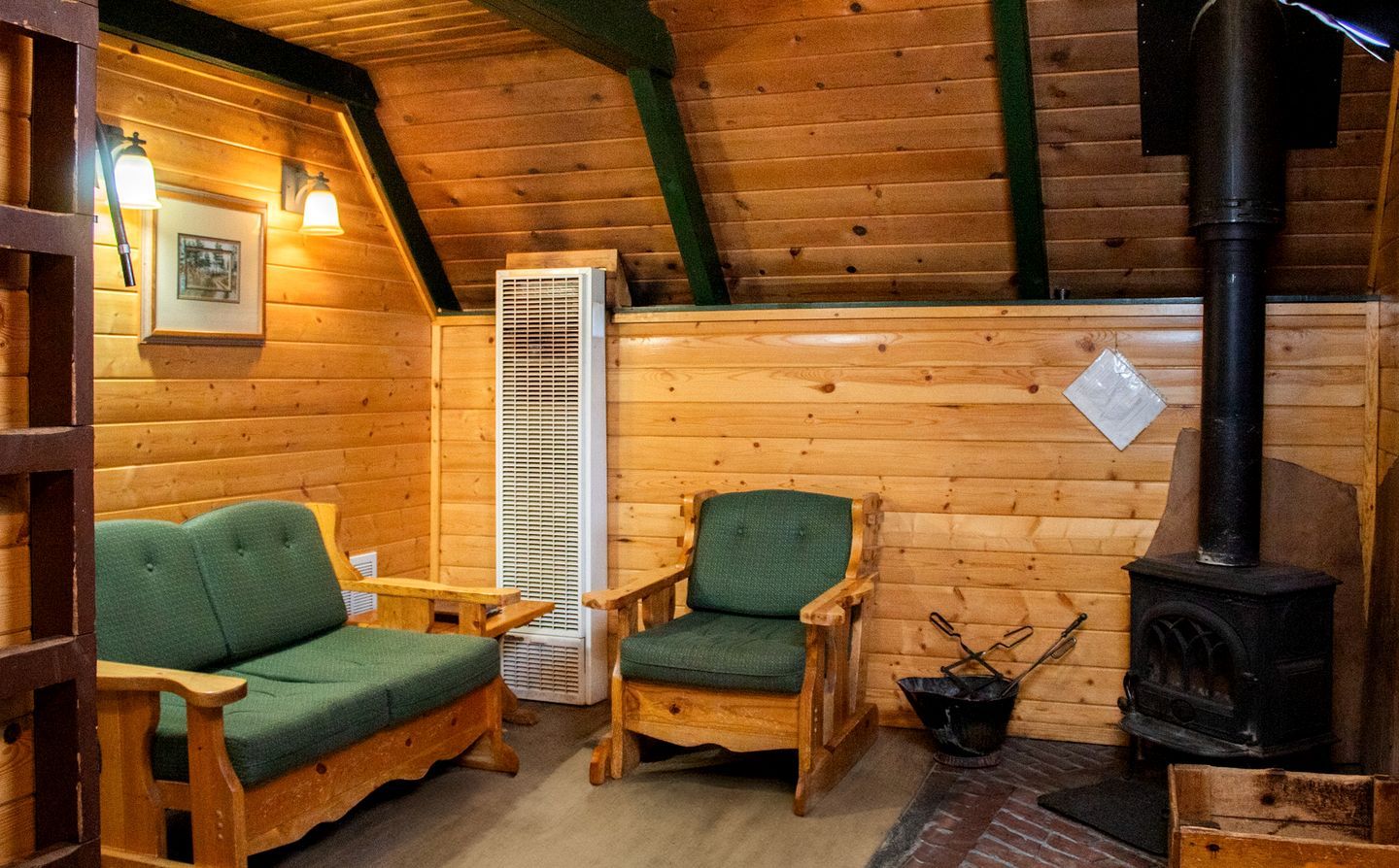 L’intérieur d’un chalet chaleureux, avec une cheminée, deux fauteuils verts, une table et un radiateur fixé au mur.