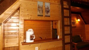 Interior de una cabaña de madera con mostrador de madera, cafetera y escalera.