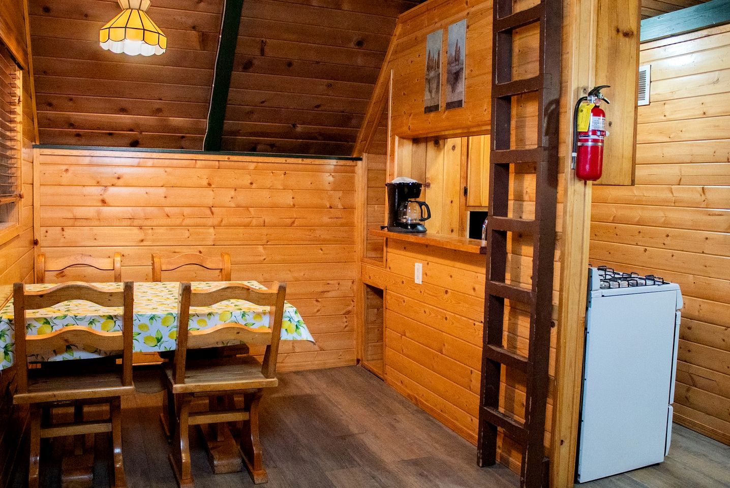 Een houten interieur met een eettafel, stoelen, een koffiezetapparaat, een koelkast en een brandblusser.