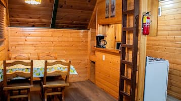 Een houten interieur met een eettafel, stoelen, een koffiezetapparaat, een koelkast en een brandblusser.