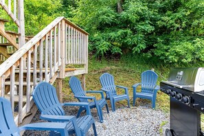 Ett trädäck med Adirondack-stolar, en grill och en trätrappa.