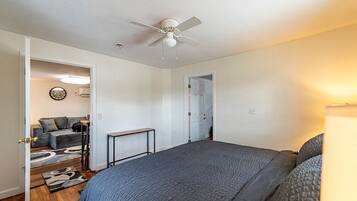 A bedroom with a bed, a ceiling fan, a door leading to another room, and a small table.