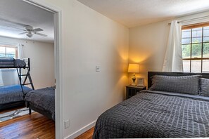 Une chambre avec un lit superposé, une table de chevet avec une lampe et une fenêtre avec des rideaux.