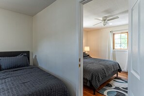 Ein Schlafzimmer mit zwei Betten, einem Deckenventilator, einem Nachttisch mit Lampe und einem Fenster mit Vorhängen.