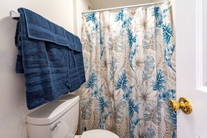 Een badkamer met een toilet, een blauwe handdoekhouder en een douchegordijn met een bladmotief.