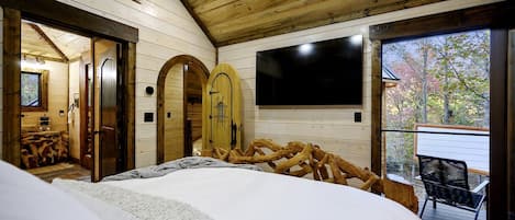 A bedroom with a large bed, wooden walls, a TV, and a balcony with a chair.