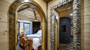 Interior de madera con una cama, el tronco de un abedul y una pared de piedra.