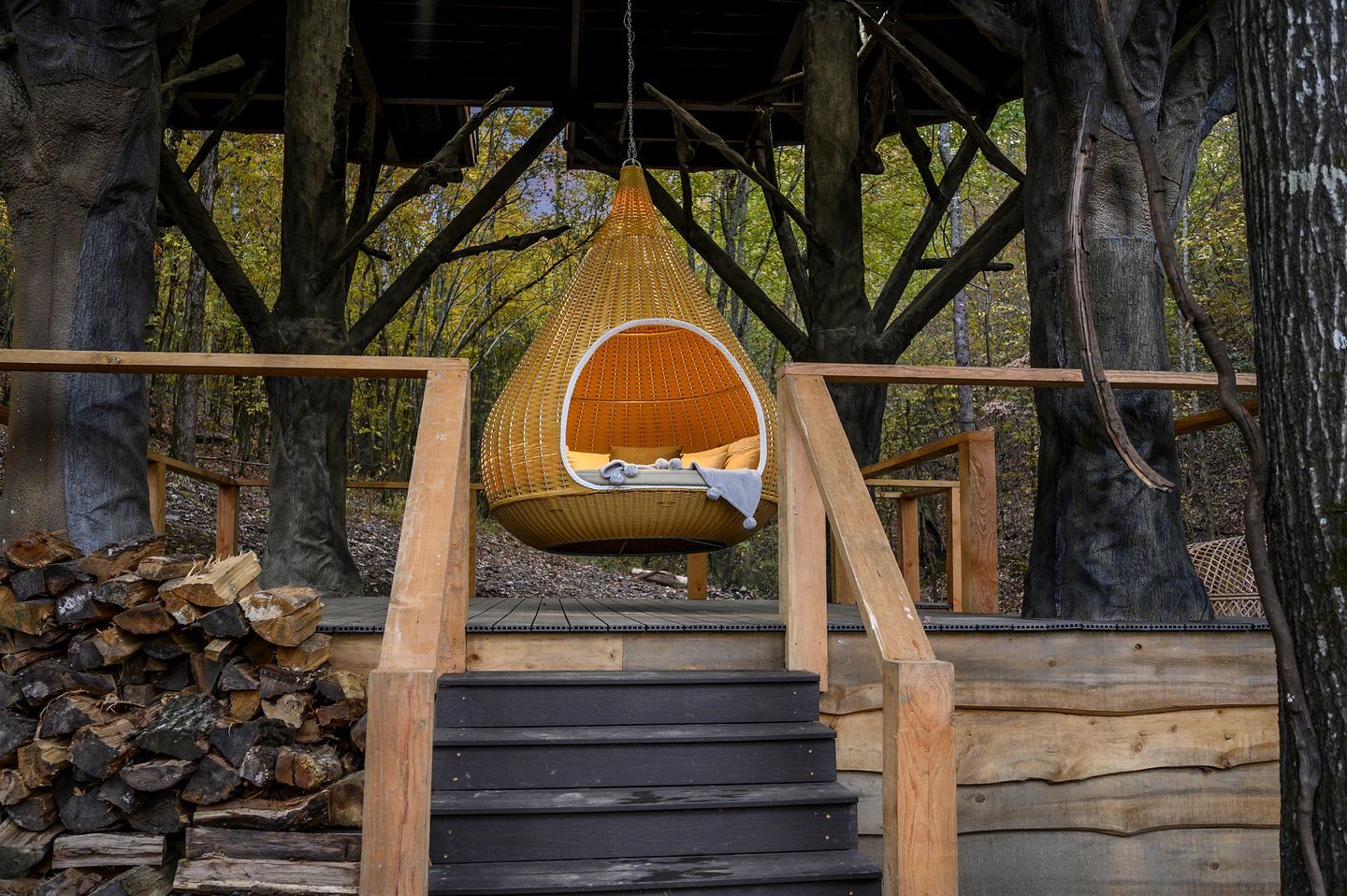 A wooden staircase leading to a hanging chair suspended from a tree.