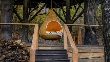 A wooden staircase leading to a hanging chair suspended from a tree.