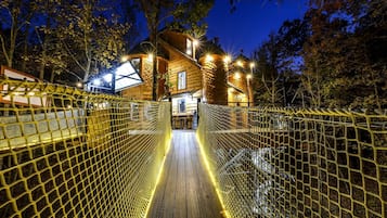 A wooden house with a bridge leading to it, surrounded by trees.