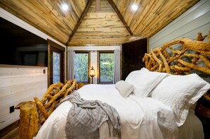 A wooden cabin interior with a bed, windows, and a view of the forest. - Gorgeous Tree House with Hot-tub in Broken Bow, Oklahoma (Broken Bow)
