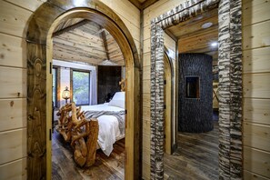 A wooden interior with a bed, a birch tree trunk, and a stone wall.