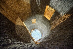 Un tragaluz circular en una habitación de paredes de piedra con una caja de madera en la pared.