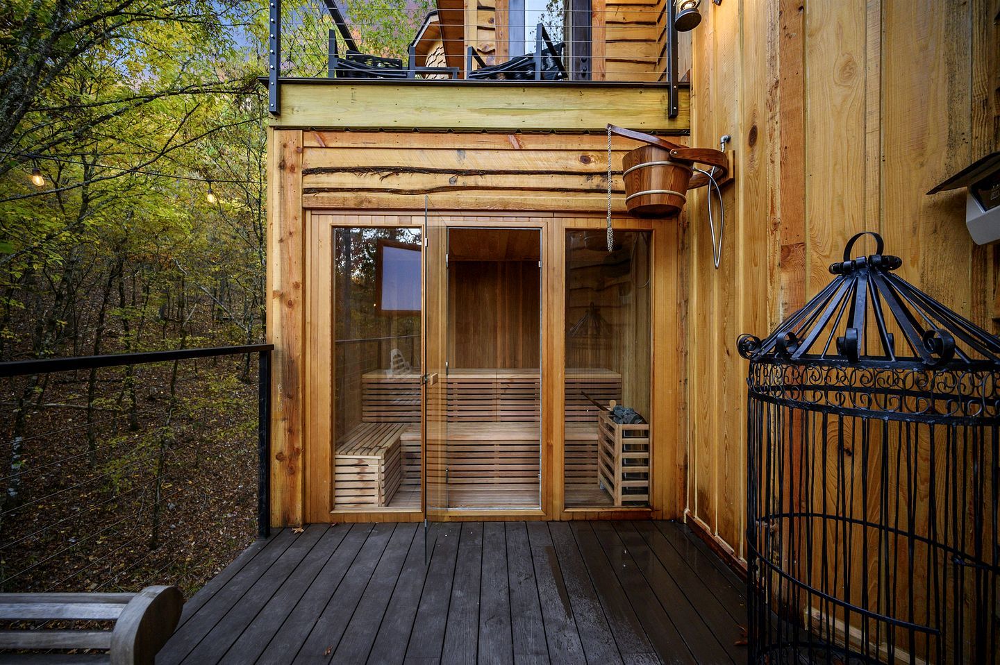 A wooden cabin with a glass door entrance, a deck, and a metal gate.