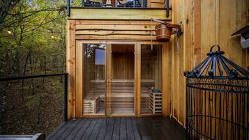 A wooden cabin with a glass door entrance, a deck, and a metal gate.