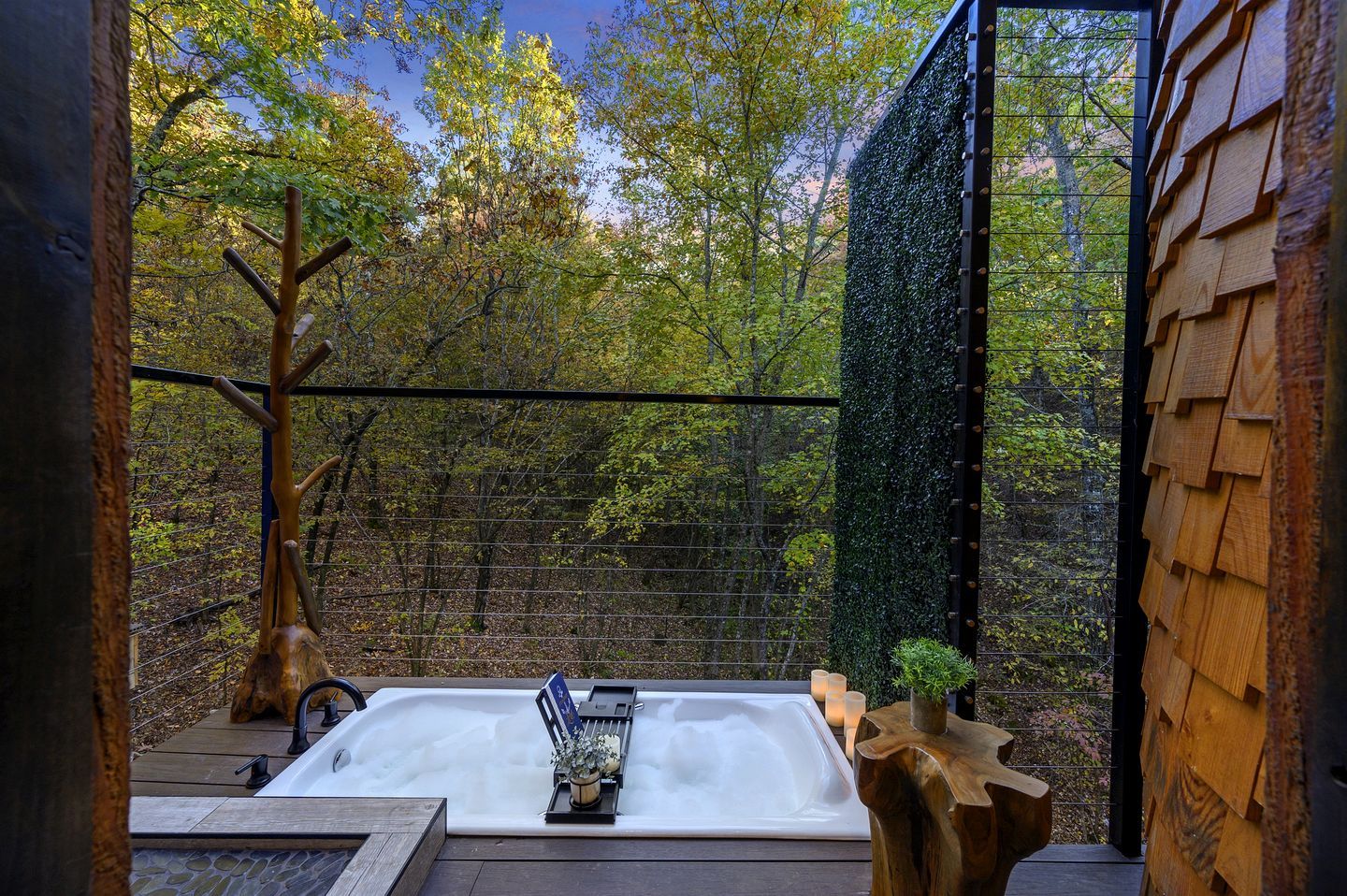 A hot tub with a view of a forest, surrounded by wooden structures and a metal fence.