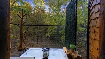 A hot tub with a view of a forest, surrounded by wooden structures and a metal fence.