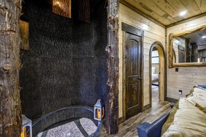 A rustic wooden room with a stone wall, a wooden door, a bed, and a mirror.