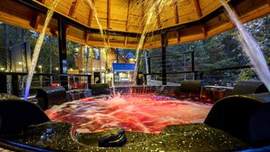 Een bubbelbad met waterstralen, omringd door houten meubels en een uitzicht op een gebouw op de achtergrond.