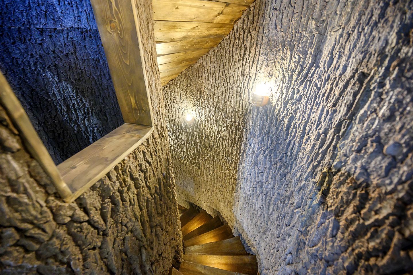 A spiral staircase in a stone-walled room with wooden beams and a small window.