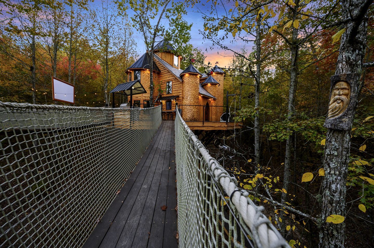 Une cabane en bois, reliée à l’extérieur par un pont de corde, et entourée d’arbres.