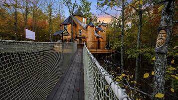 A wooden cabin with a rope bridge leading to it, surrounded by trees.