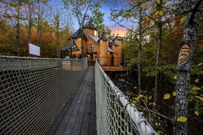 A wooden cabin with a rope bridge leading to it, surrounded by trees.