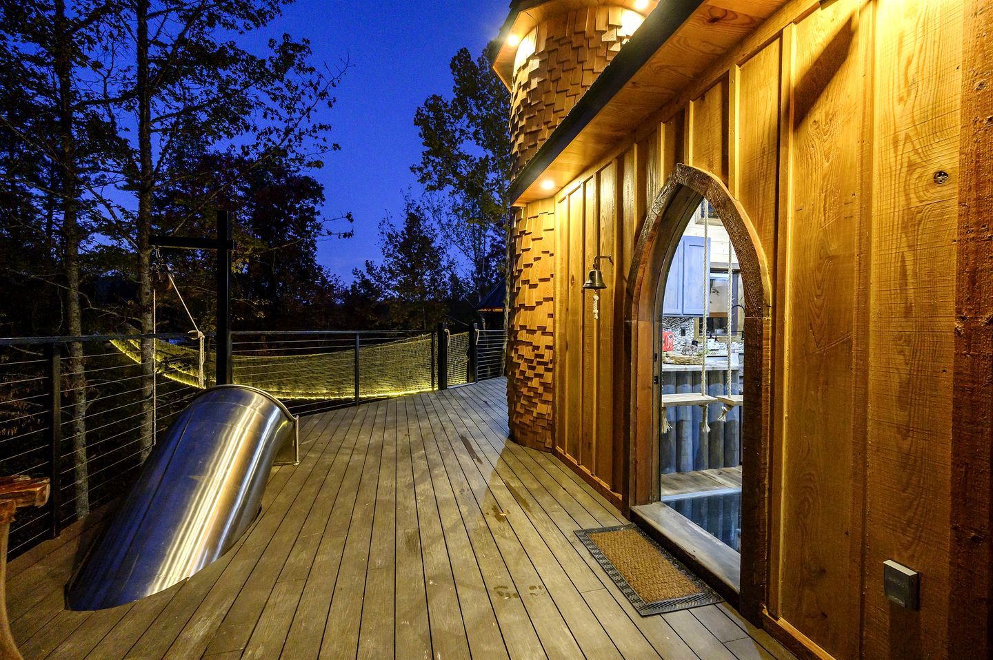 Une terrasse en bois avec une porte vitrée donnant sur un espace piscine, le tout entouré d’arbres.