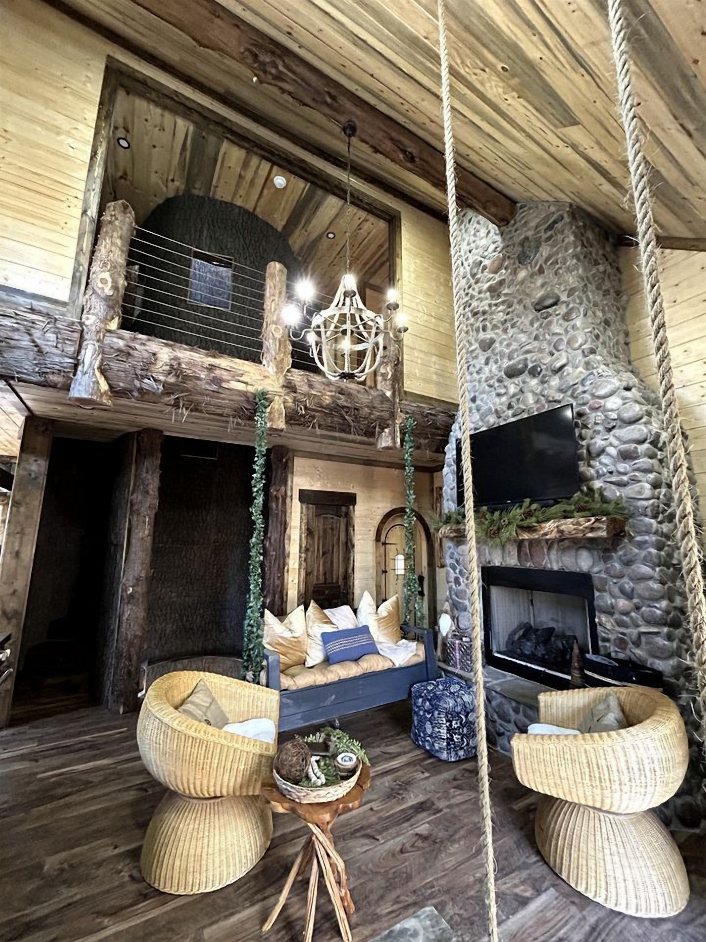 A rustic interior with a stone fireplace, a hanging light fixture, and a wooden ceiling.
