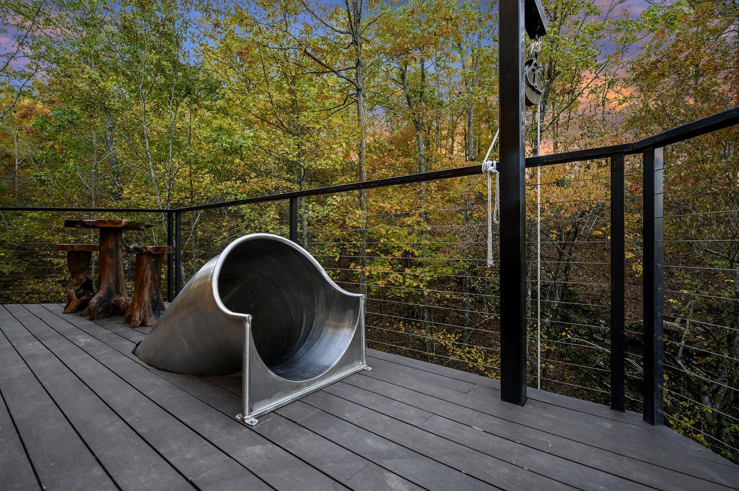 A wooden deck with a metal slide and rustic wooden tables.
