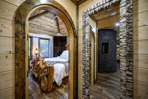 Interior de madera con una cama, el tronco de un abedul y una pared de piedra.