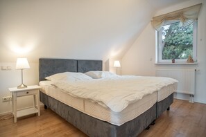Un dormitorio con cama, lámparas de noche, una ventana con cortinas y un radiador.