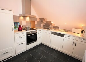 Een kleine keuken met witte kasten, een inbouwoven, een vaatwasser en een spoelbak.
