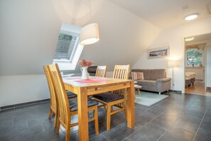 A dining area with a wooden table and chairs, a window with a view, and a ceiling light. - Apartment 'Haus K 102 OG' with Private Garden, Balcony and Wi-Fi (Röbel)